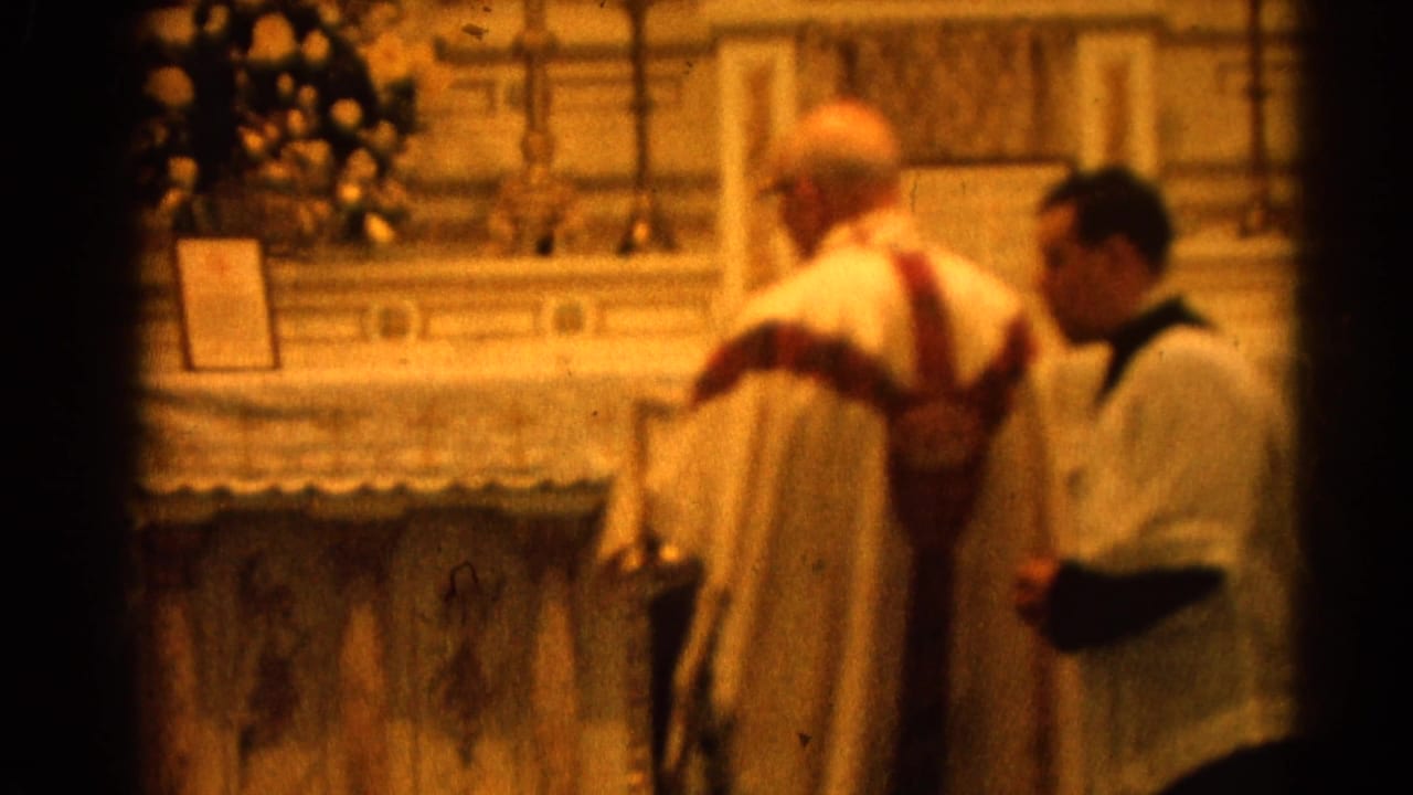 Priest in white and red vestments stands near an altar server at a church altar.