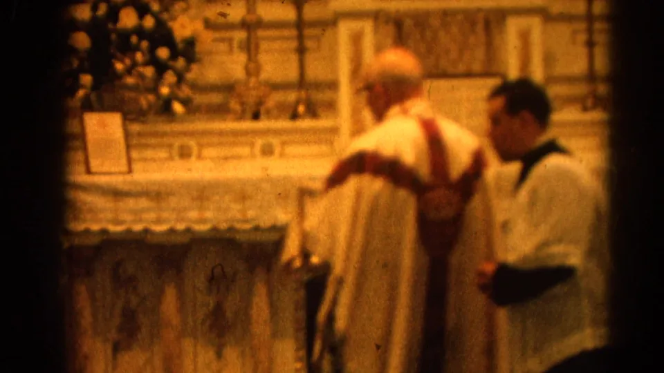 1964 Harvard, Illinois home-movie frame showing a Catholic priest and altar server near an ornate church altar.