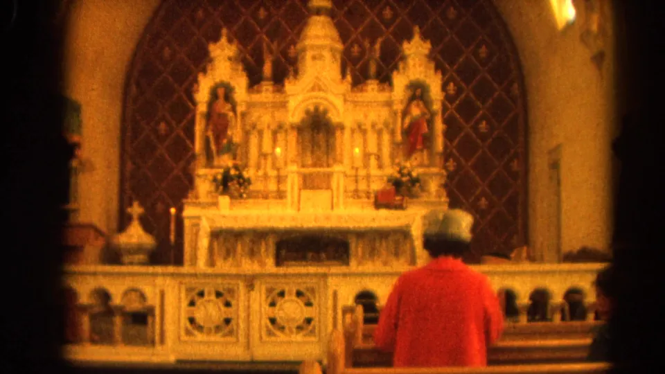 1964 Harvard, Illinois church interior with a person viewed from behind near the altar rail, facing statues, candles, and a white altar.