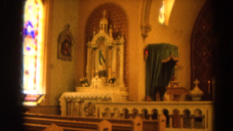 1964 Harvard, Illinois 8mm view of a side altar, stained glass window, pews, candles, and a green-draped religious statue.
