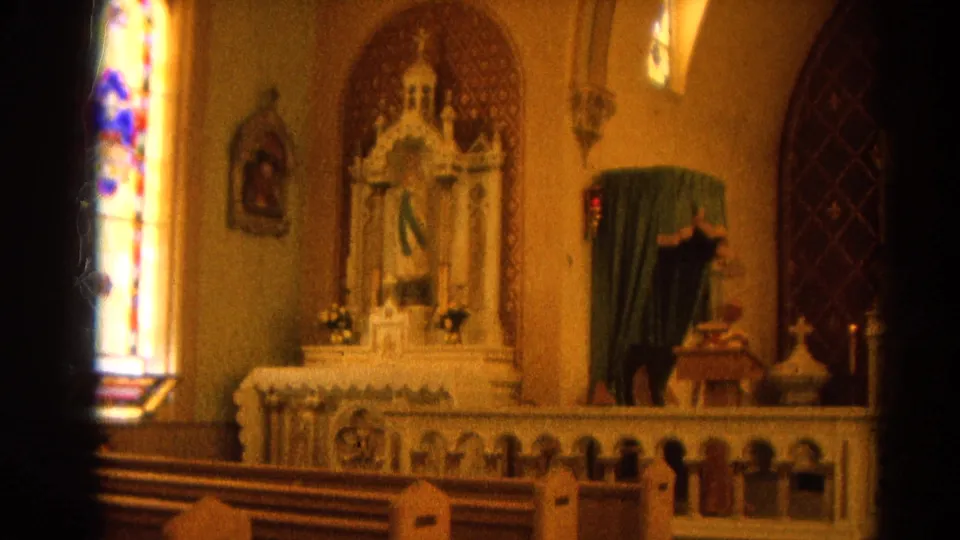 1964 Harvard, Illinois church frame showing pews, stained glass, altar rail, candles, and a green-draped statue at a side altar.