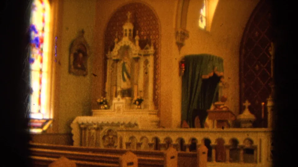 1964 Harvard, Illinois church interior showing an altar, stained glass window, pews, and religious statuary from a handheld 8mm view.
