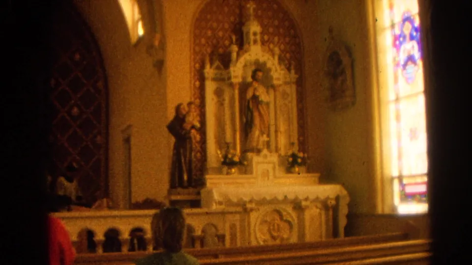 Harvard, Illinois Catholic church interior with altar statuary, stained glass, pews, and a person partly visible from behind in 1964 8mm footage.