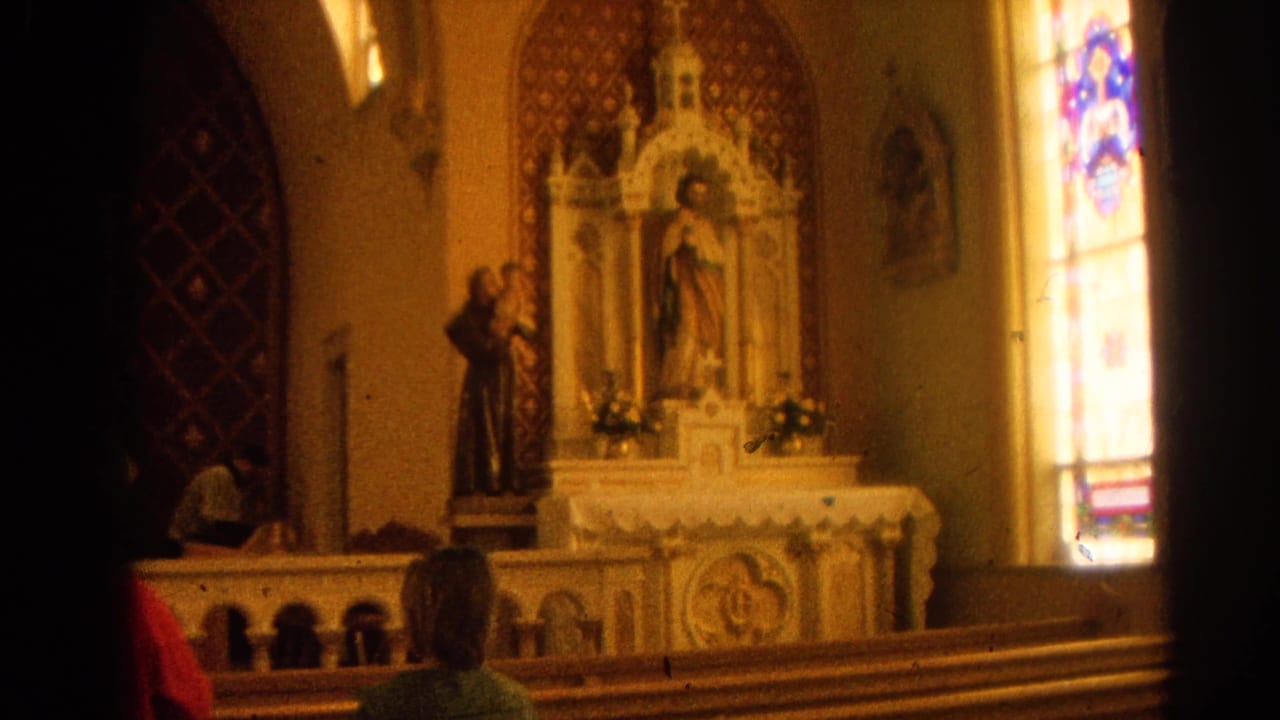 Ornate church altar with statues, stained glass, pews, and seated parishioners.