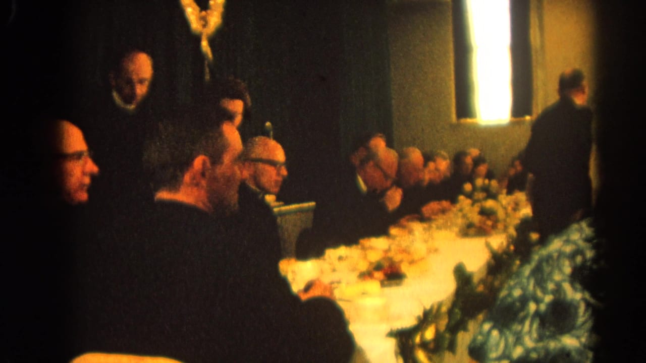 Men in dark suits seated around a long banquet table in a dim formal room.