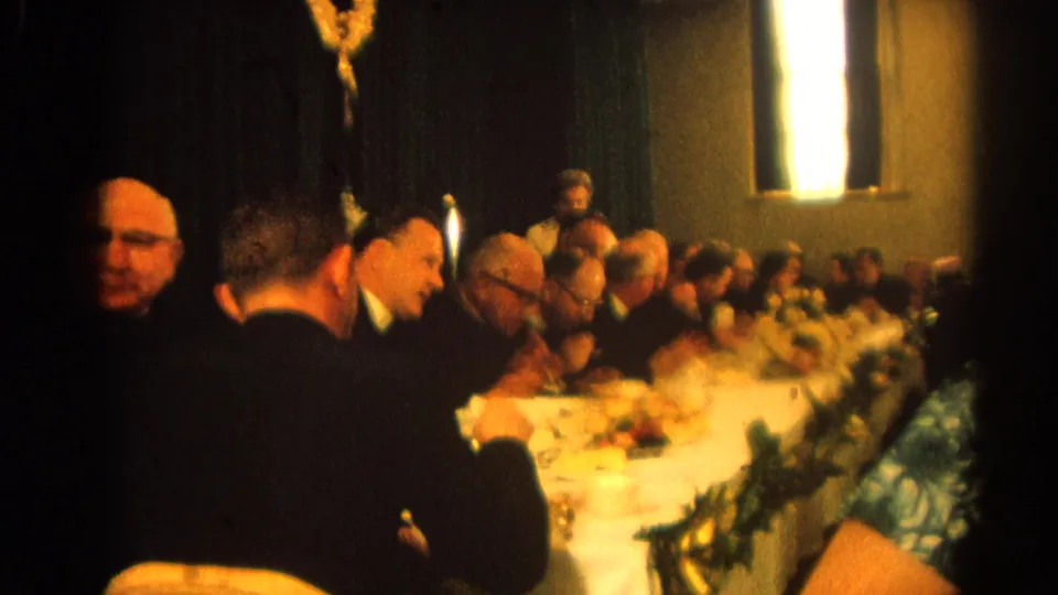 Warm 8mm frame of suited guests and clergy eating at a formal dinner in Harvard, Illinois in 1964.