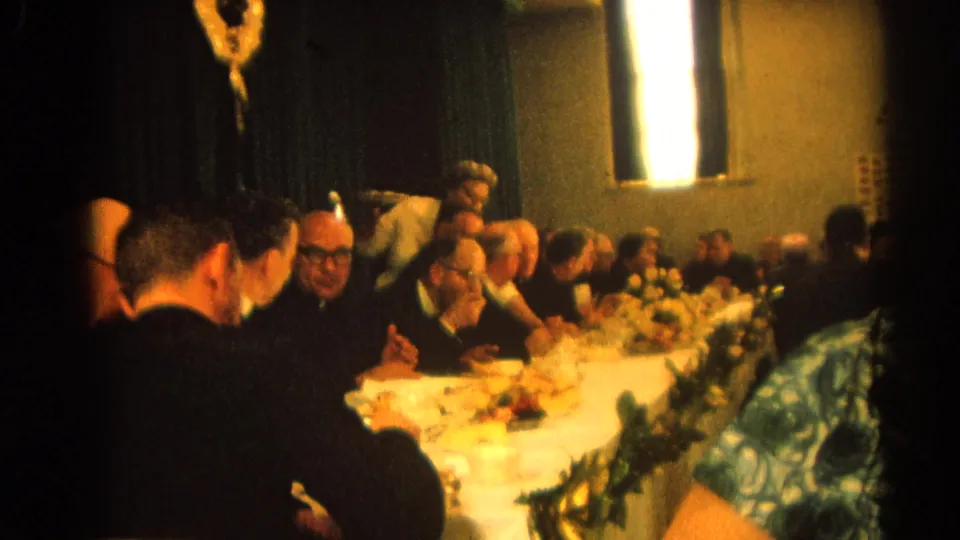 Handheld 1964 home-movie view down a hotel banquet table with clergy and guests dining in Harvard, Illinois.