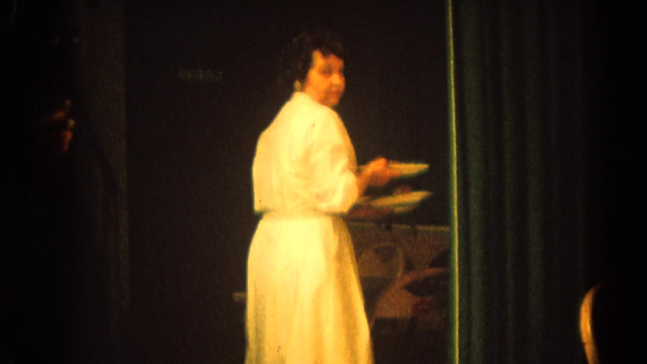 Woman in a white dress carrying plates near a banquet table in a dim hall.