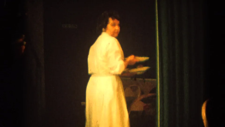 In Harvard, Illinois 1964 home-movie footage, a woman in white appears to serve food beside a long table during a formal clergy or family meal.