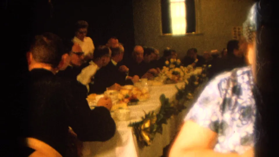 Harvard, Illinois 1964 footage shows clergy and formal guests seated along a white tablecloth with flowers, plates, and cups in a warm interior.