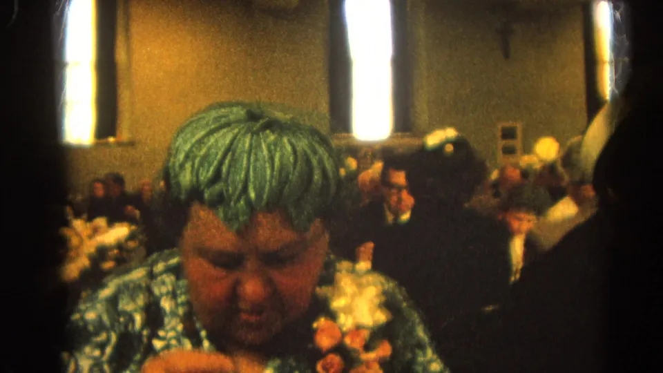 Close 8mm view of the woman in a green patterned dress eating during a 1964 luncheon or banquet in Harvard, Illinois.