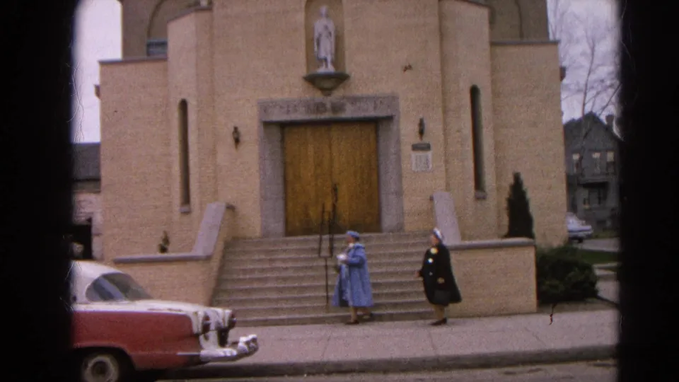 Final 1964 Harvard, Illinois frame with two women on the sidewalk before a tan church and a red mid-century car.