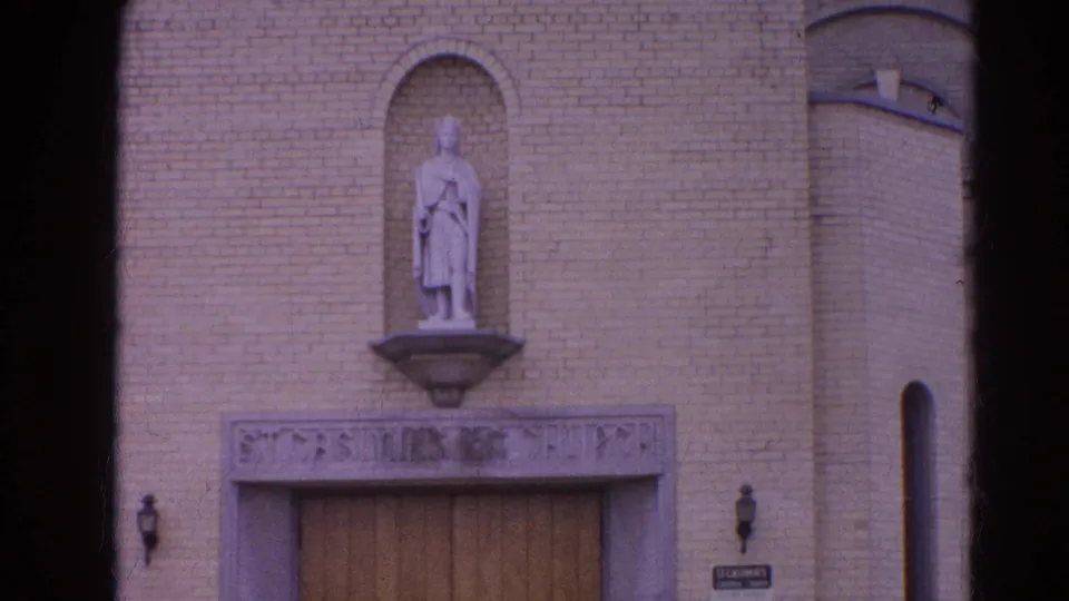 Closer 1964 Harvard, Illinois view of the church entrance, showing brickwork, a statue niche, wooden doors, and a small sign.