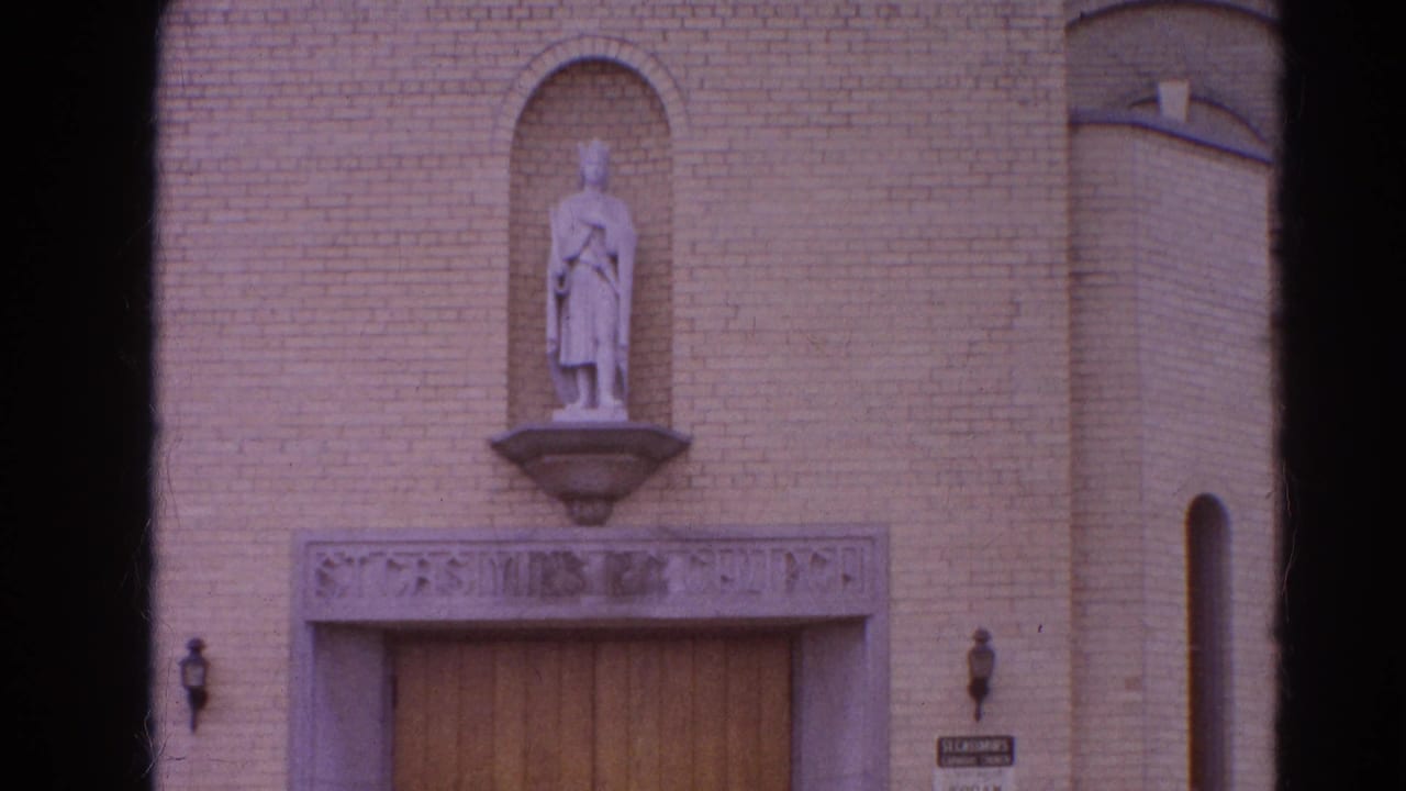 Brick church entrance with a robed statue in an arched niche above wooden doors.
