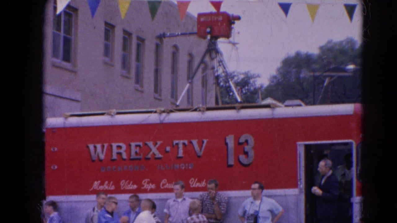 Red WREX-TV 13 mobile unit parked beside a street crowd under colorful pennants.