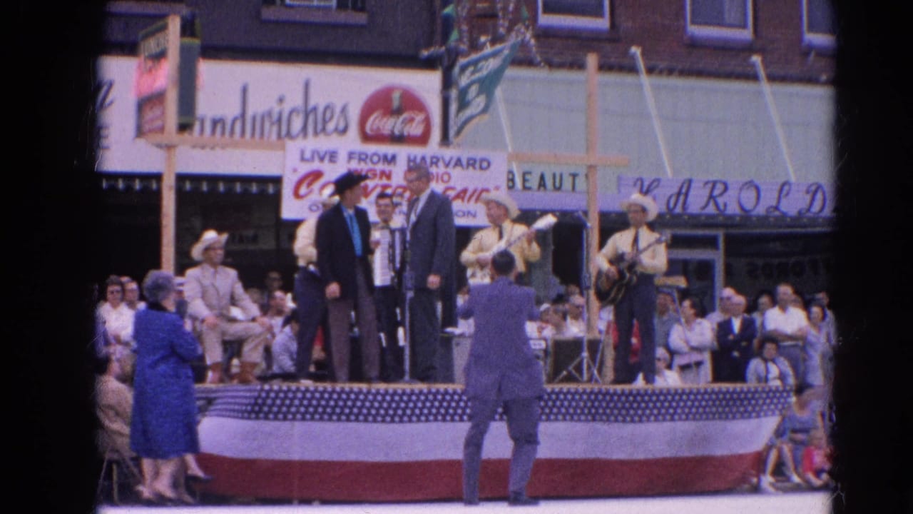 Outdoor stage with country musicians, suited speakers, crowd, and radio fair signage.