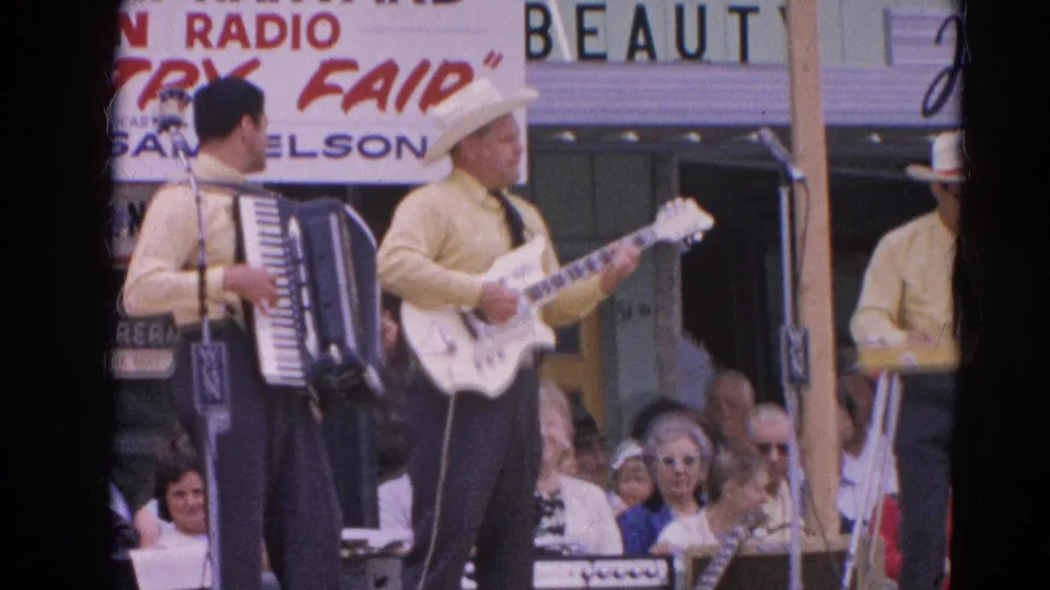 Country musicians in matching shirts perform at the 1964 Harvard, Illinois fair as a crowd watches from behind the stage area.