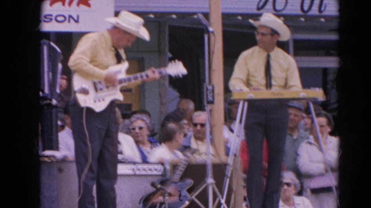 Two men in cowboy hats perform on an outdoor stage with white electric guitar and keyboard before a seated crowd.