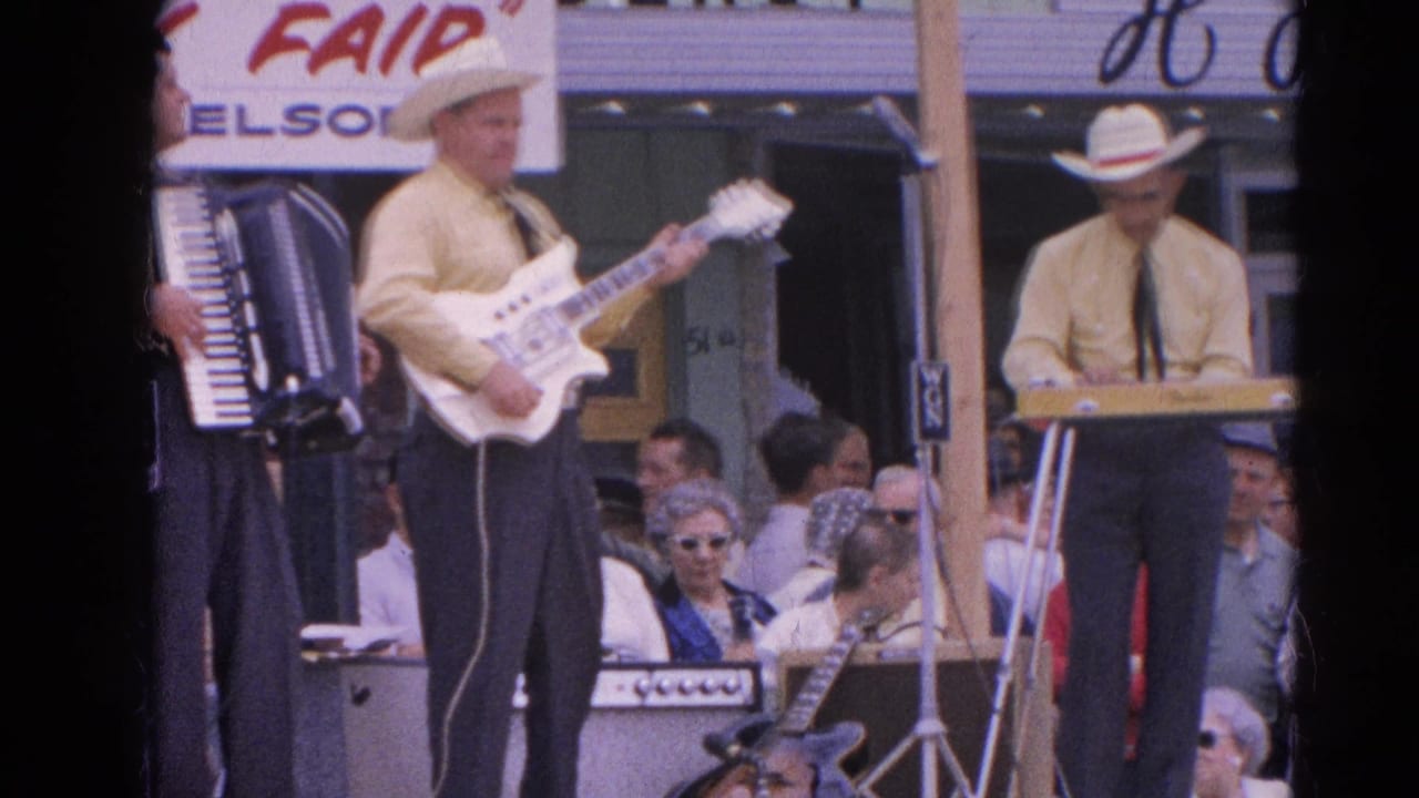 Country band members in cowboy hats perform on an outdoor stage before seated spectators.