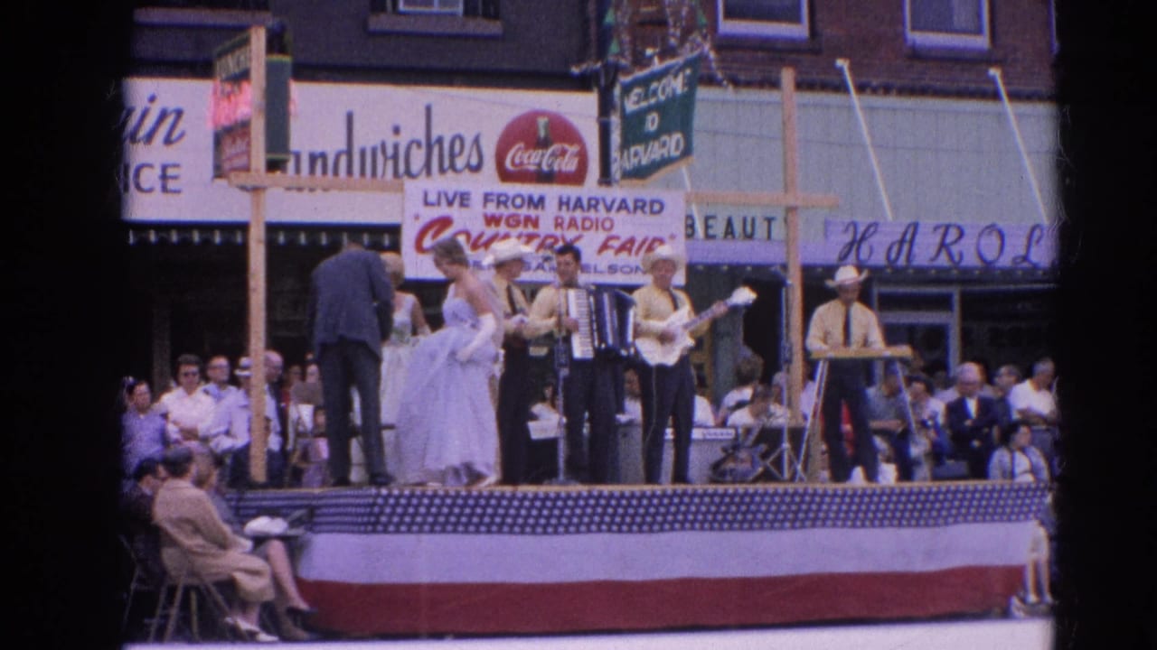 Street stage with musicians, dancers, bunting, storefront signs, and seated spectators.