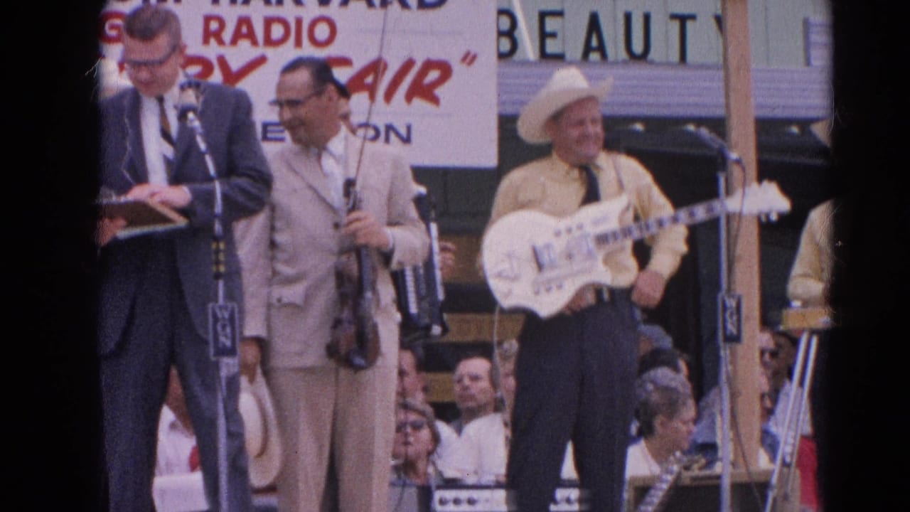 Suited announcer at microphones beside country musicians under a radio fair banner.