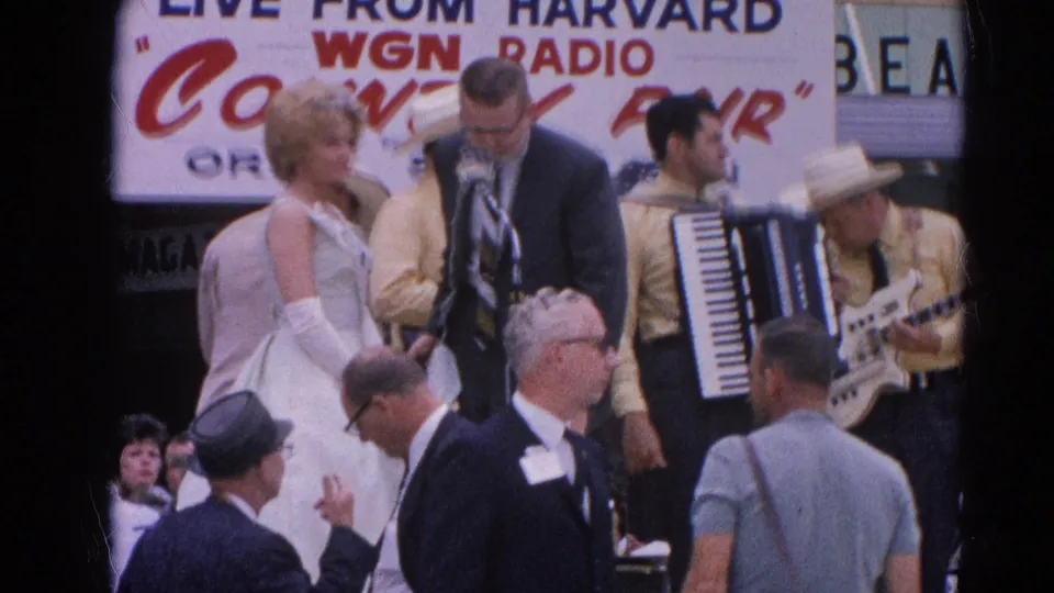 The singer and suited host face the microphones with accordion and guitar players behind them at the 1964 country fair in Harvard, Illinois.