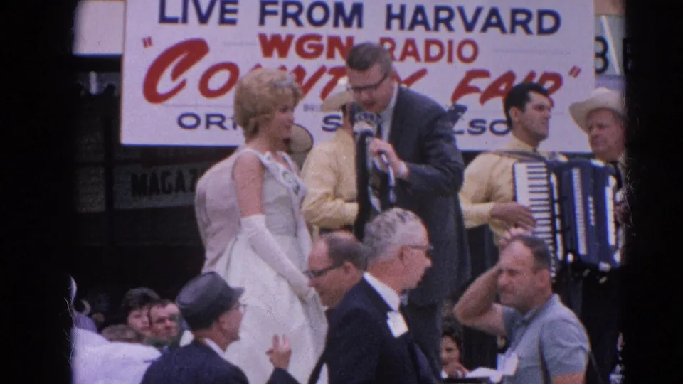 The camera frames the singer, host, accordion player, WGN Radio signage, and adult spectators at the Harvard, Illinois country fair performance.