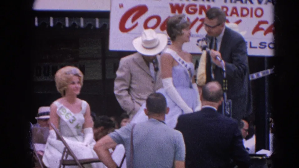 At the 1964 Harvard, Illinois fair presentation, a standing pageant contestant is framed with announcers, a seated participant, and WGN Radio signage.