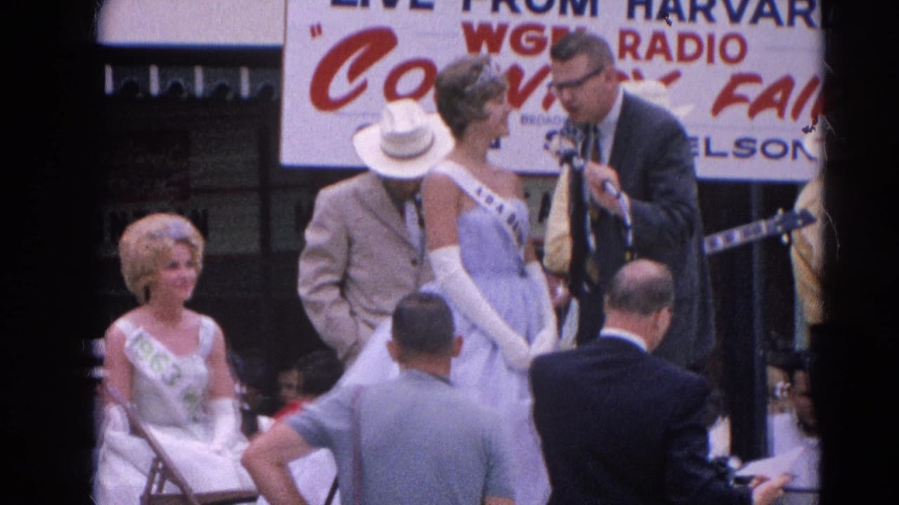 Pageant contestant in blue gown interviewed on a fair stage beneath a WGN Radio banner.