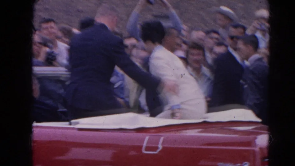 Close parade view from Harvard, Illinois in 1964 as a suited man greets a woman in a light dress beside the red convertible.
