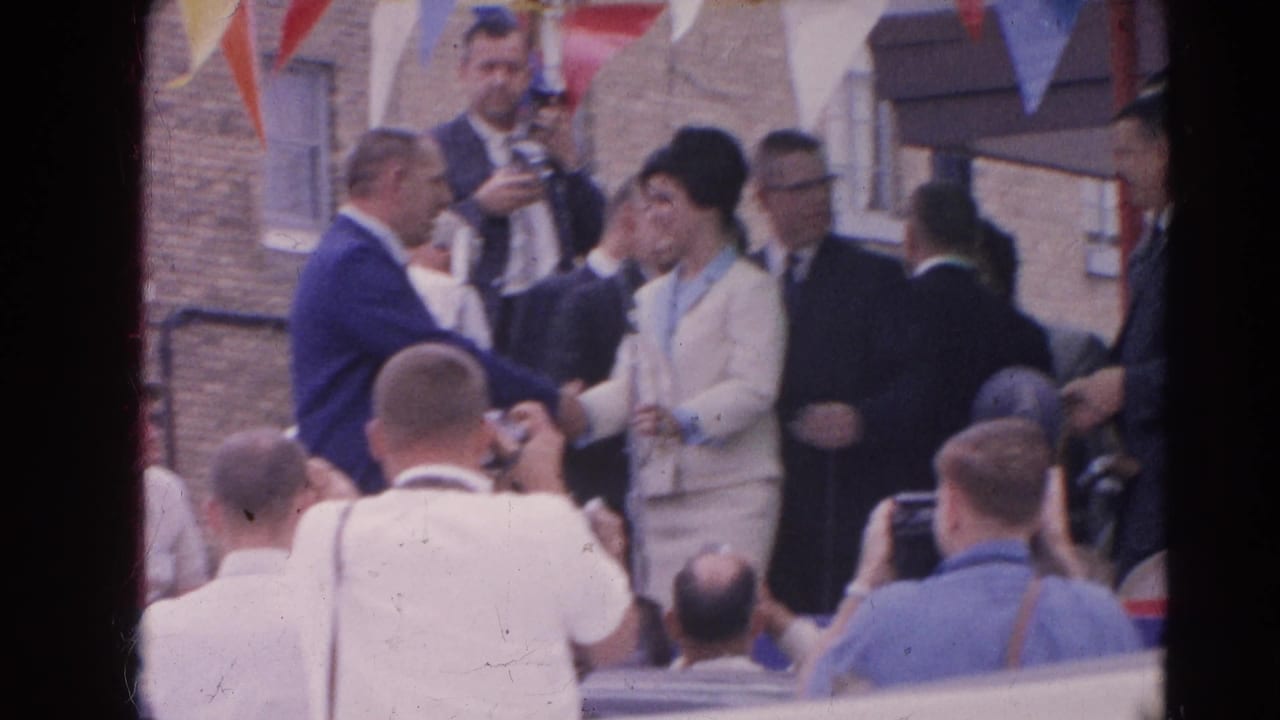 At a 1964 Harvard, Illinois public event, a woman in a pale suit and dark hat stands before microphones with press and suited men nearby.