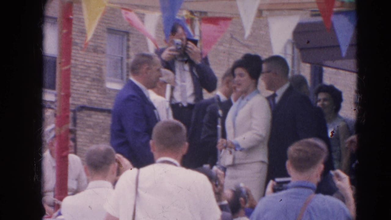 The 1964 Harvard, Illinois scene shows a woman in a pale suit near microphones, watched by photographers, suited men, and spectators.