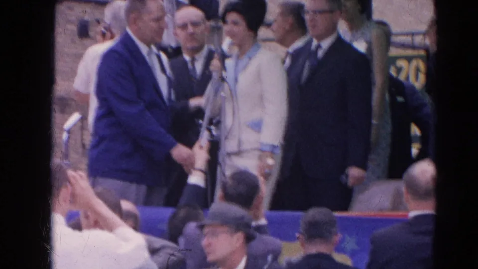The final frame shows the 1964 Harvard, Illinois public platform with the woman, suited men, microphones, and spectators in front.