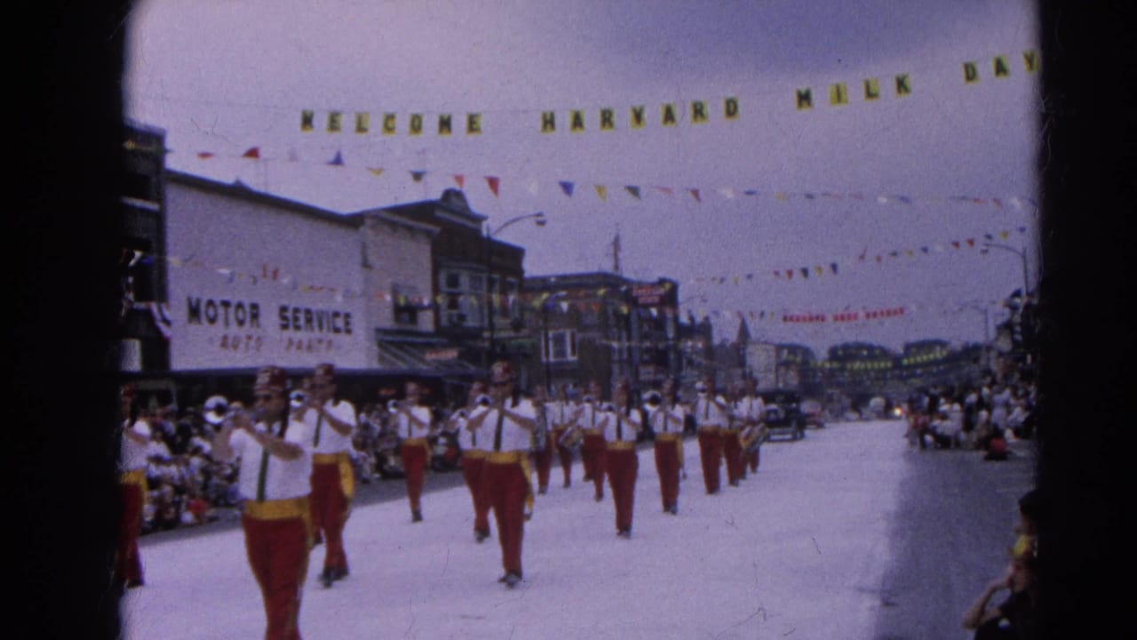Uniformed band members march toward the camera with spectators lining the street.