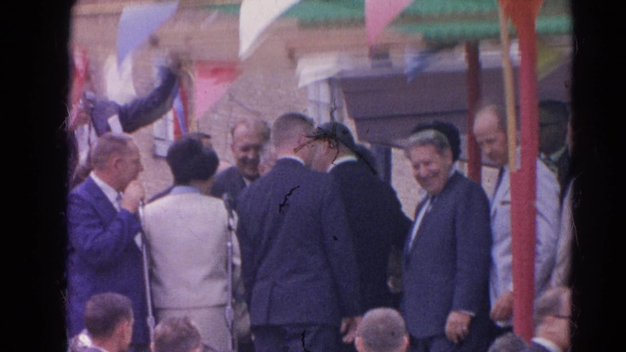 Outdoor Harvard, Illinois gathering with suited men, spectators, bunting, and a partially turned speaker near the platform.