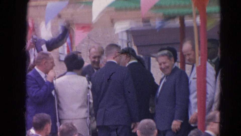 Outdoor Harvard, Illinois gathering with suited men, spectators, bunting, and a partially turned speaker near the platform.