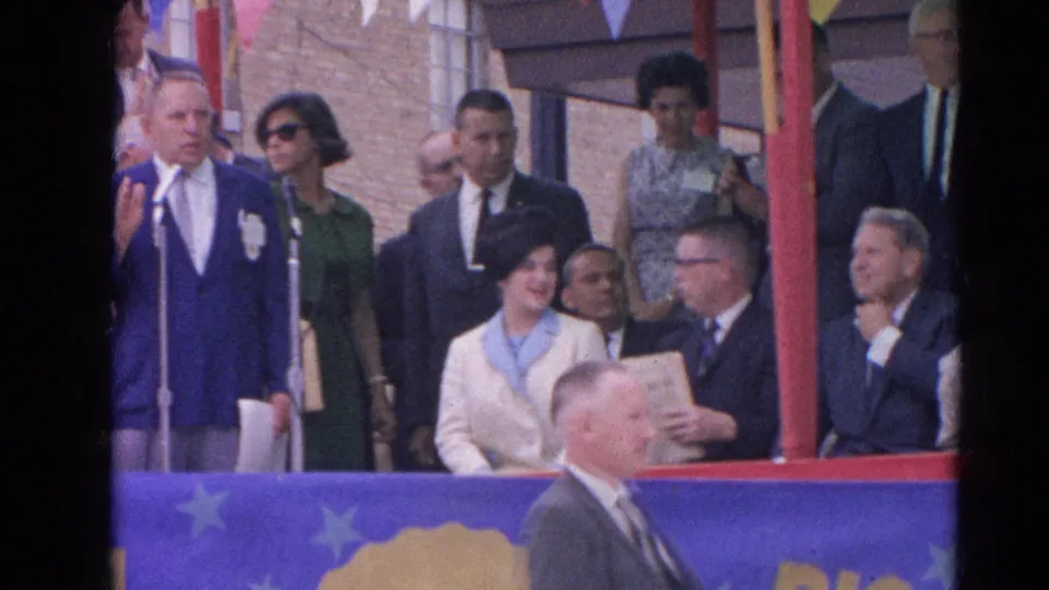 The 1964 Harvard, Illinois platform scene shows the speaker, a woman in sunglasses, and seated attendees during the outdoor ceremony.