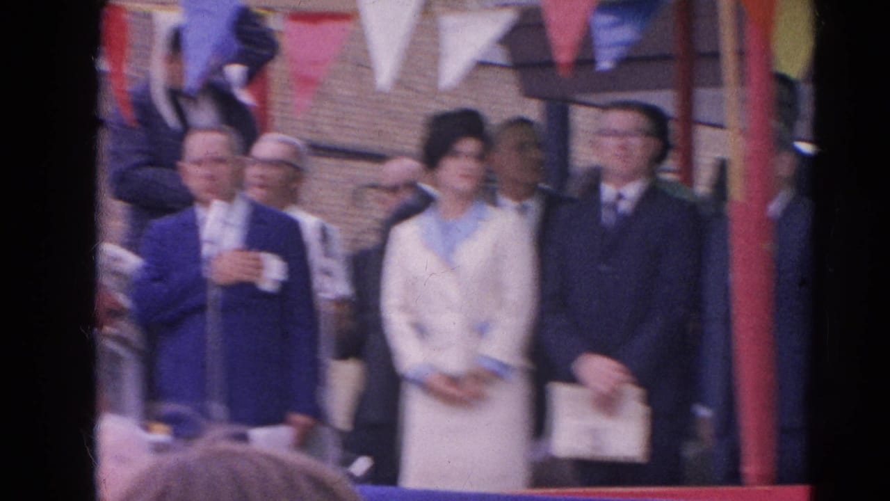1964 Harvard, Illinois frame with a man in a blue suit near microphones and formally dressed people under bunting.
