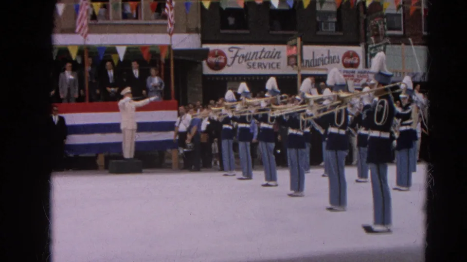 The final frame shows the band lined up in the street during the 1964 Harvard, Illinois ceremony, with storefronts, bunting, spectators, and Coca-Cola signage visible.