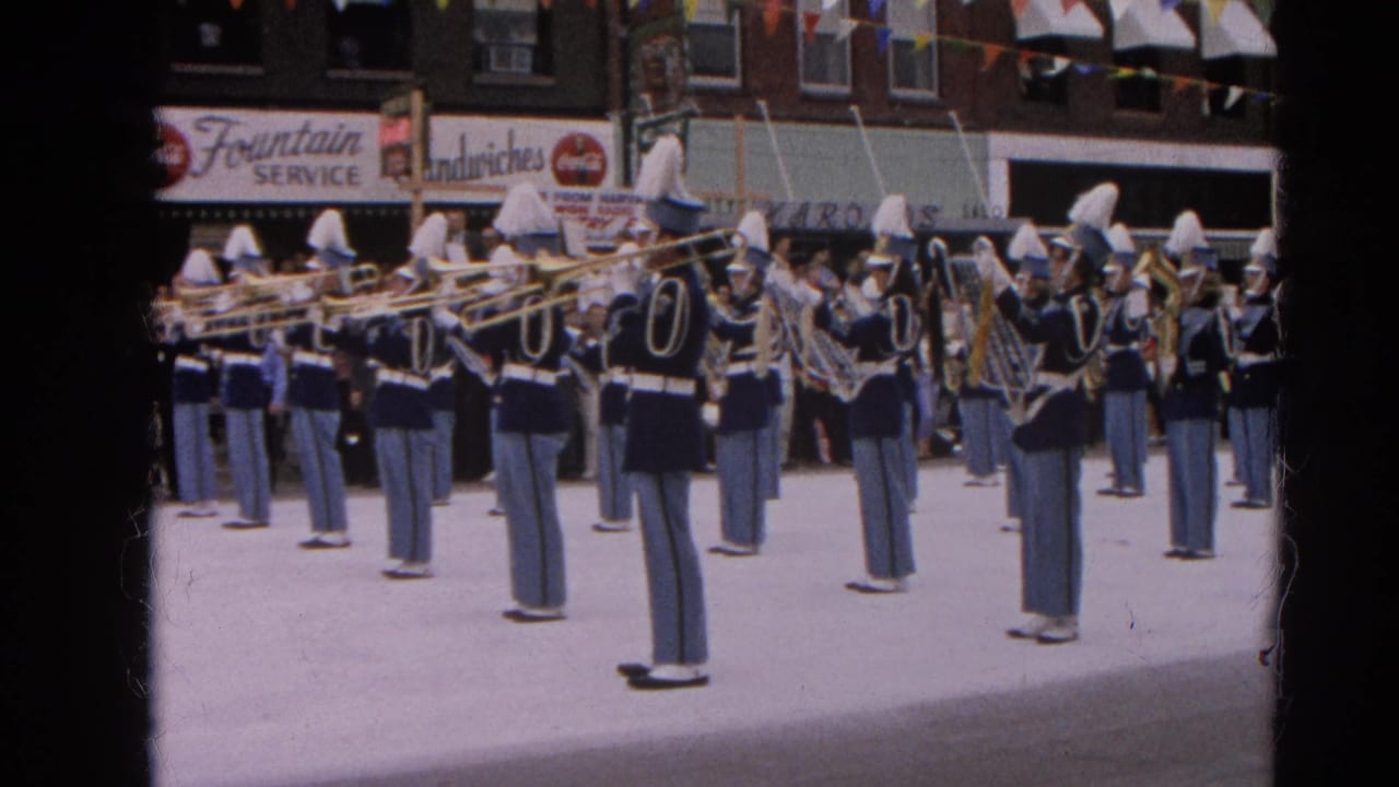Marching band in blue uniforms plays brass instruments on a decorated town street.