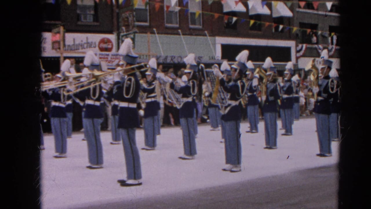 Harvard, Illinois parade band stands in formation with trombones and tubas under storefront signage and overhead bunting.