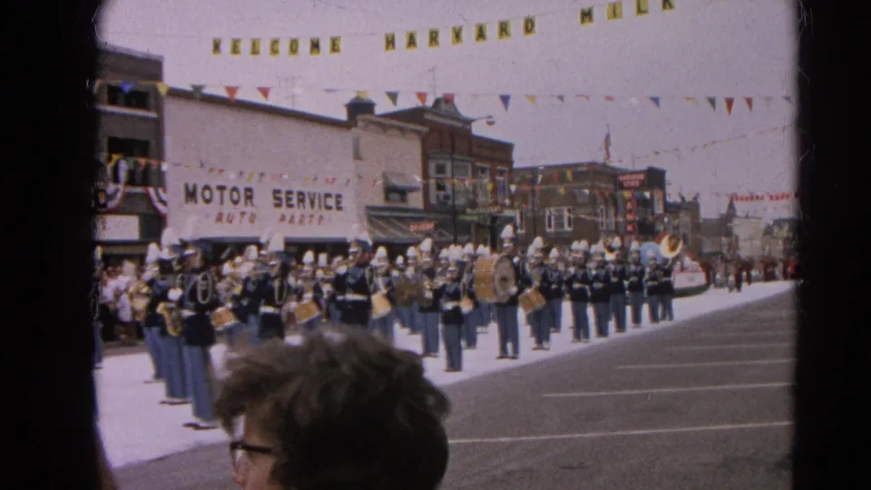 Wide 1964 Harvard, Illinois parade view showing the band across the street beneath a Welcome Harvard banner and bunting.