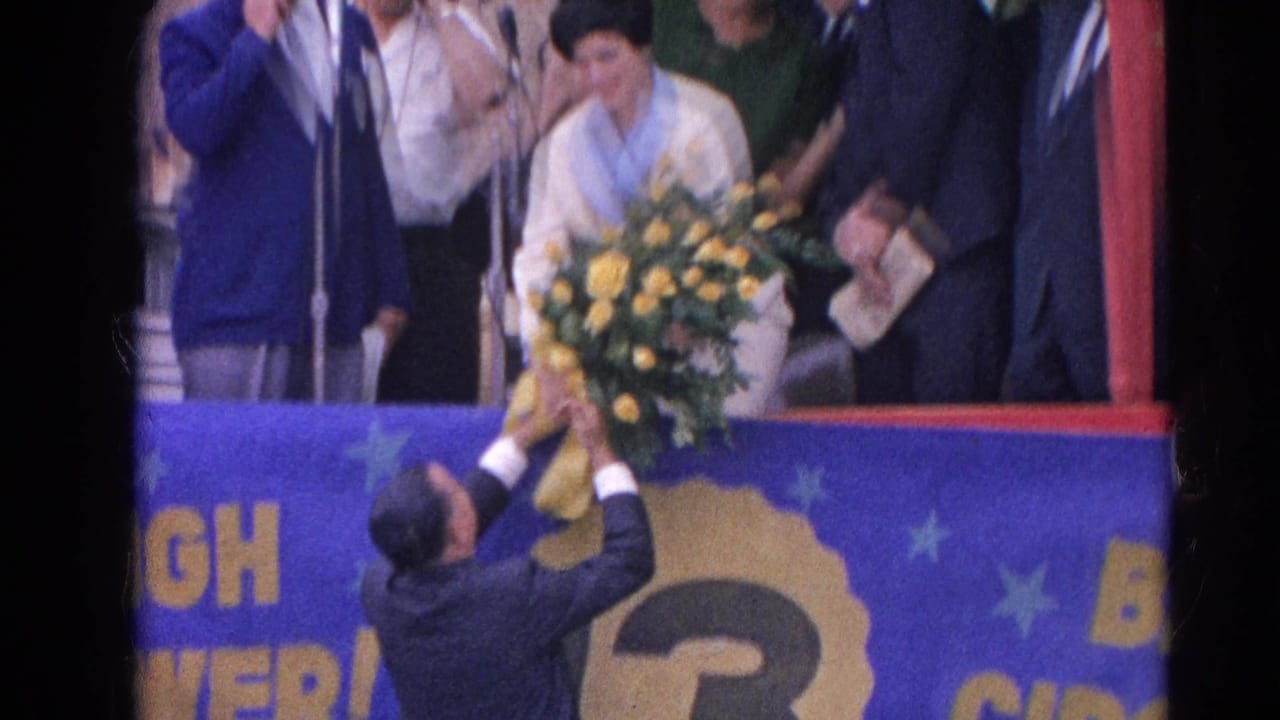Woman on decorated stage receives a large bouquet from a man below.