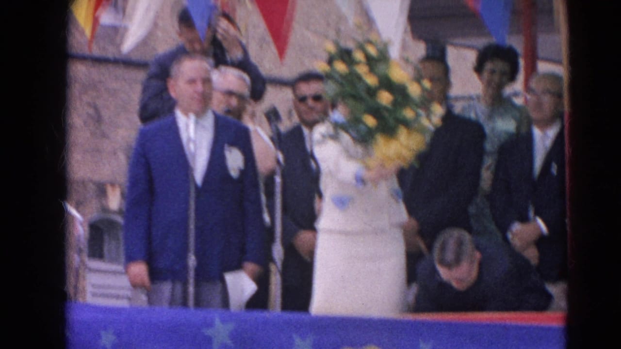 Woman holding a large bouquet stands beside a man in a blue jacket at an outdoor ceremony.