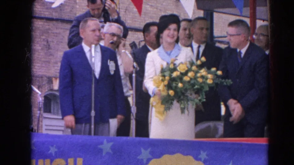 The Harvard, Illinois 1964 footage shows a woman with yellow flowers flanked by suited men during an outdoor presentation.
