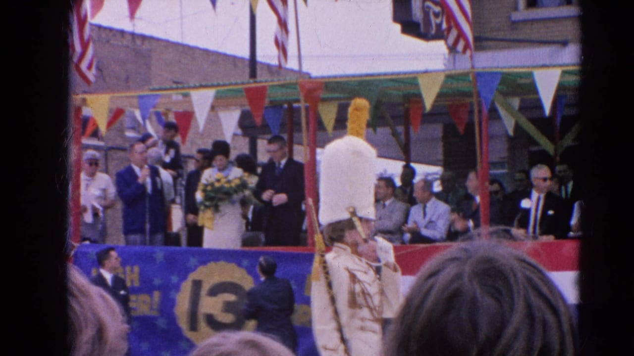 A 1964 Harvard, Illinois parade float carries formally dressed people while American flags and bunting hang above the watching crowd.