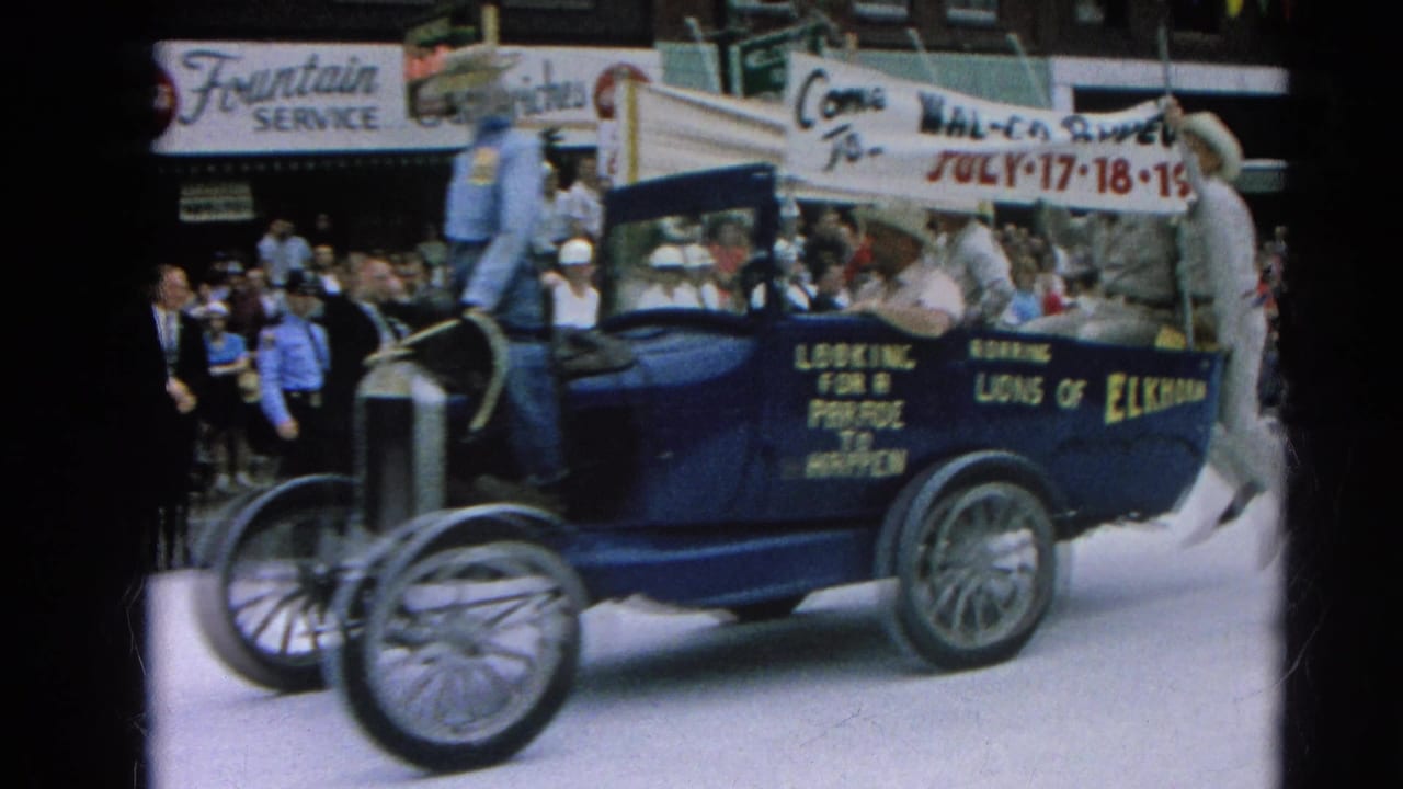 Blue open parade car with riders and a Wal-Co Rodeo banner passing spectators.