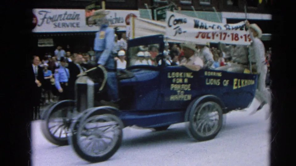 1964 Harvard, Illinois parade scene with a blue open car marked Roaring Lions of Elkhorn and a rodeo banner above the riders.