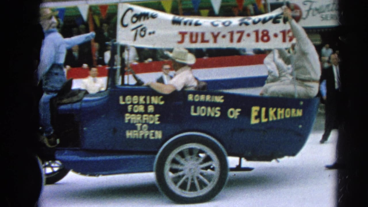 Side view of the blue parade car with riders, bunting, and rodeo banner.