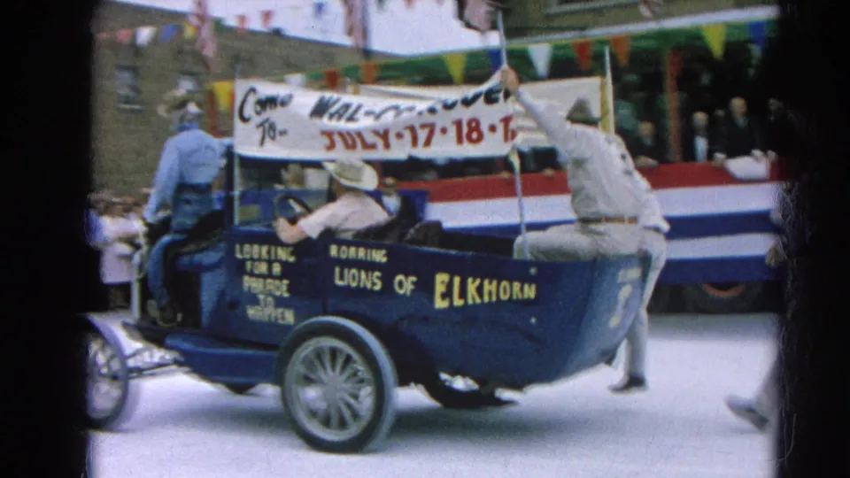 Harvard, Illinois parade frame showing the blue Roaring Lions of Elkhorn car from the rear side as a rider steadies the Wal-Co Rodeo banner.